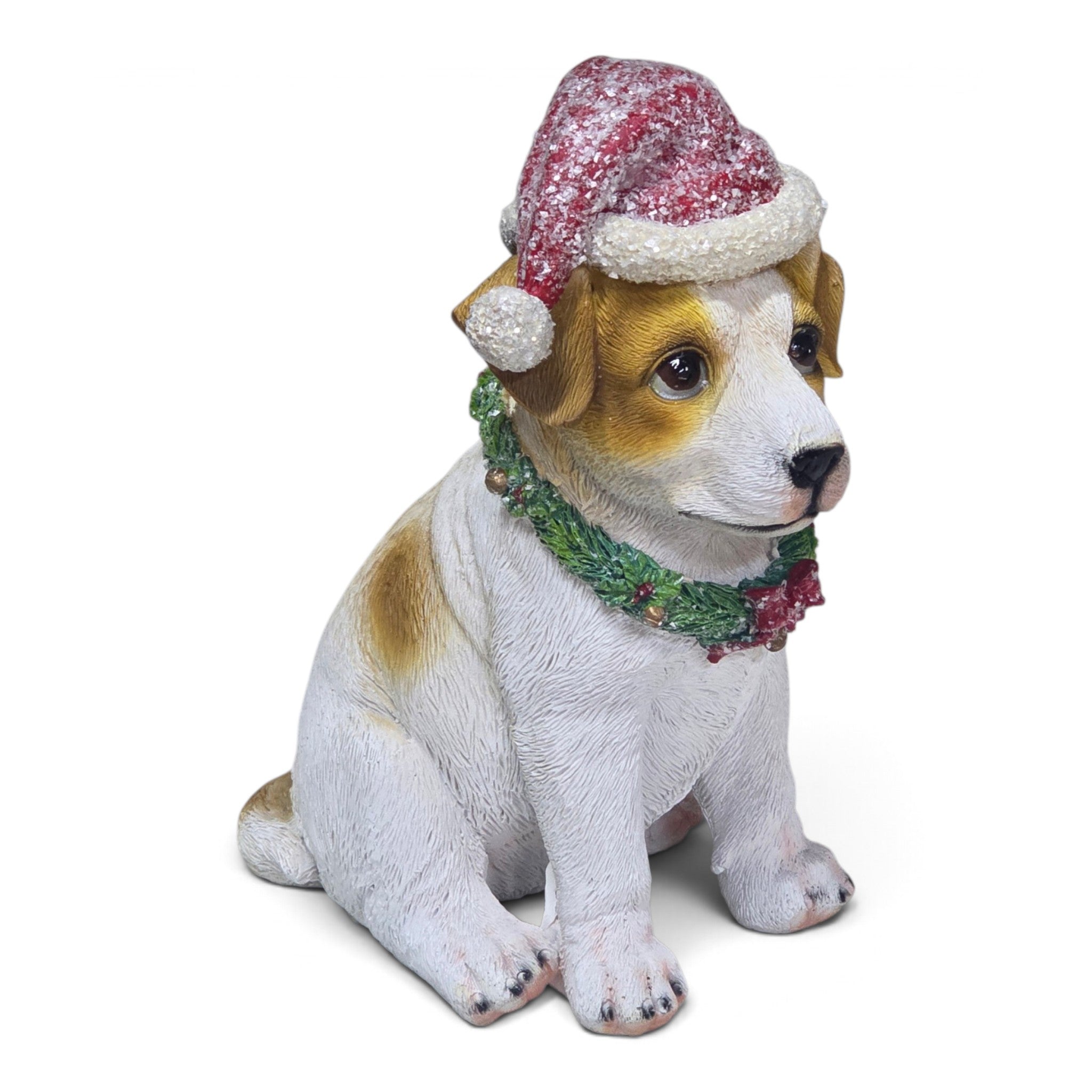 A sitting dog figurine or garden statue with a white and tan coat, wearing a red and white Santa hat and a green garland with red berries, photographed on a plain white background.