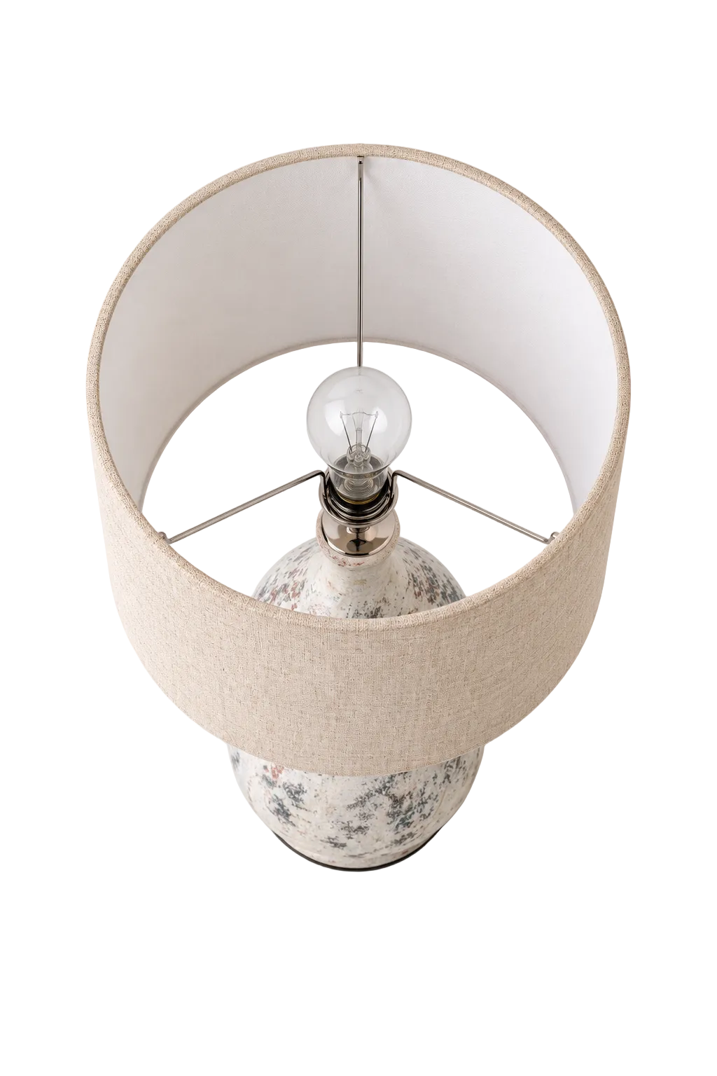 A table lamp with a large beige fabric drum shade, a clear glass bulb, and a white ceramic base with a delicate blue floral pattern, shown against a light gray background.