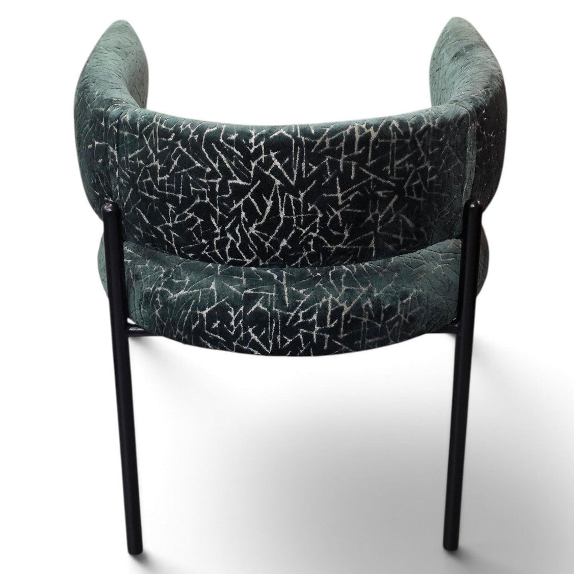 A modern accent chair with a curved backrest and seat, upholstered in a dark teal-green velvet fabric with a white crackle or crackled pattern, supported by slim black metal legs, shown from a rear three-quarter angle on a white background.