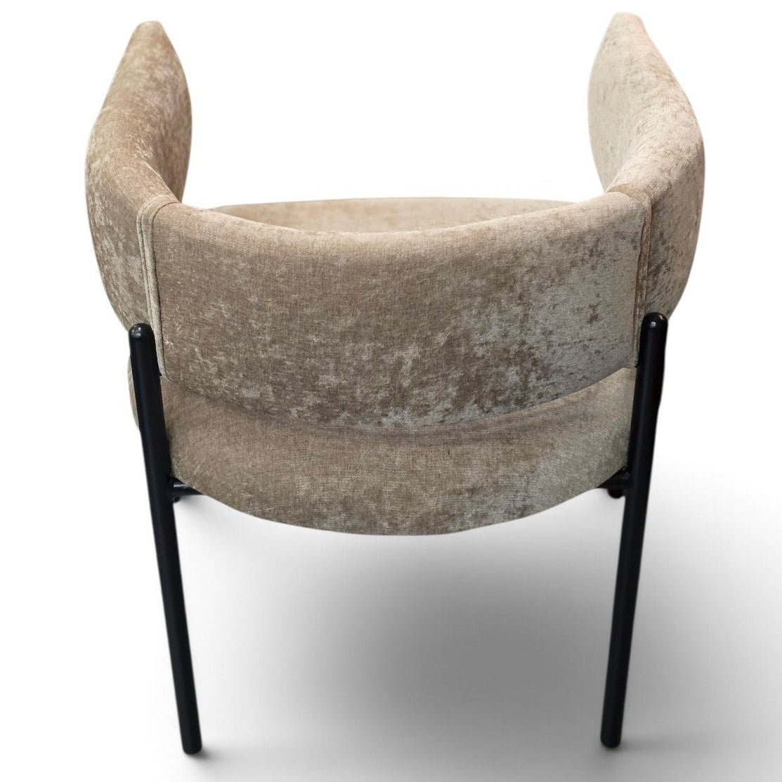 A modern accent chair with a curved, cushioned backrest and arms upholstered in a textured beige velvet fabric, supported by slim black metal legs, shown from a rear three-quarter angle on a white background.