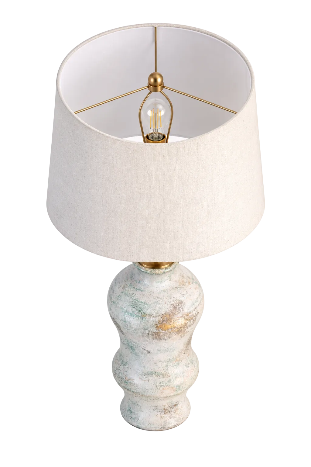 A table lamp with a textured, distressed ceramic base in off-white, light blue, and gold tones, topped with a large cream-colored fabric drum shade and a visible clear bulb.