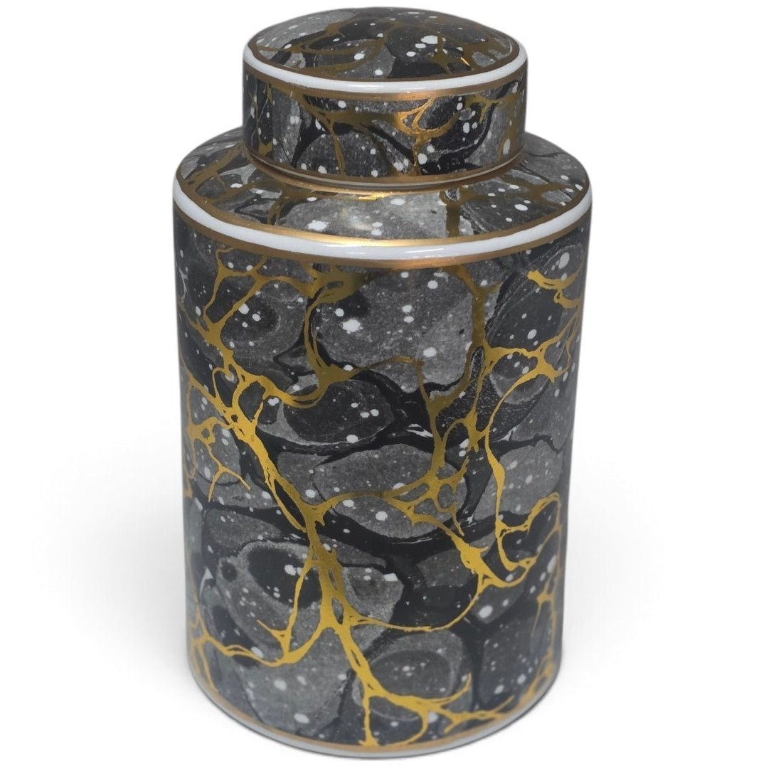 A cylindrical ceramic jar with a matching lid, featuring a black and gray marble pattern accented with gold veins and white speckles, set against a plain white background.